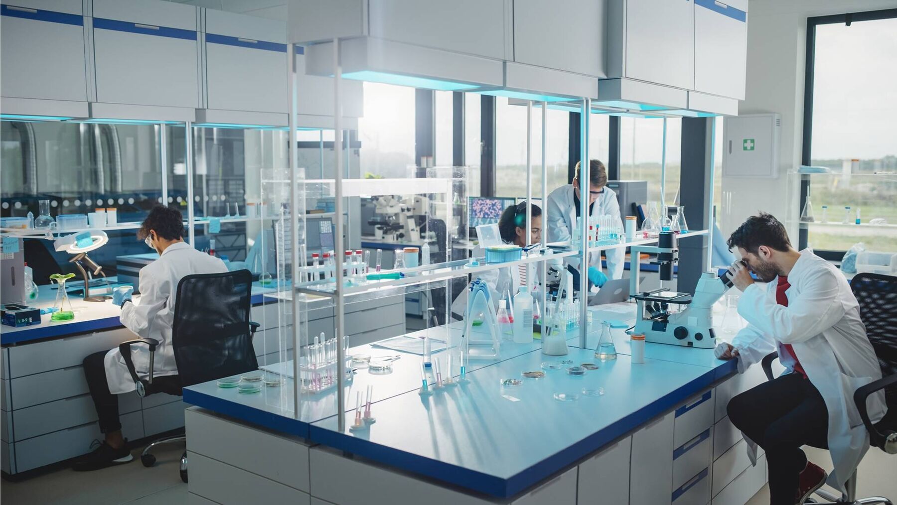 Modernes Forschungslabor mit Laborzeilen, Mikroskopen und arbeitenden Wissenschaftlerinnen und Wissenschaftlern
